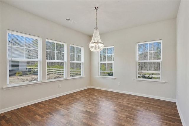 unfurnished room with dark wood-type flooring, an inviting chandelier, visible vents, and baseboards