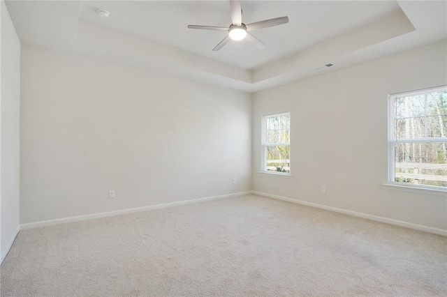 unfurnished room with a tray ceiling, light colored carpet, visible vents, ceiling fan, and baseboards