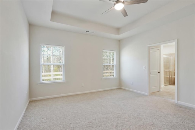 spare room with a tray ceiling, a healthy amount of sunlight, and visible vents