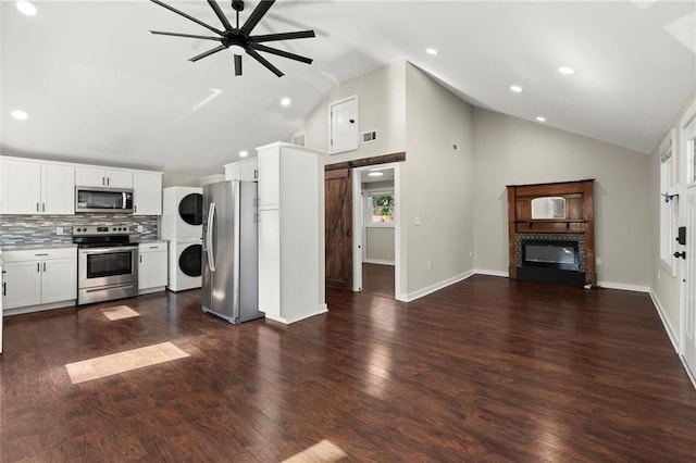 kitchen featuring a barn door, stacked washer / drying machine, stainless steel appliances, light countertops, and white cabinetry