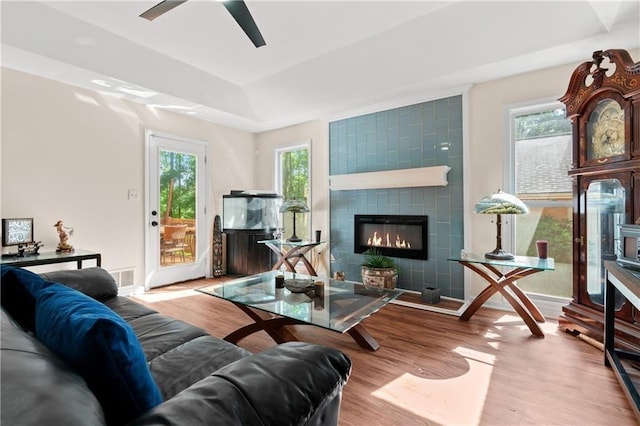 living room with ceiling fan, a tiled fireplace, light hardwood / wood-style floors, and a healthy amount of sunlight