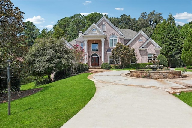 view of front of home featuring concrete driveway, brick siding, a chimney, and a front yard