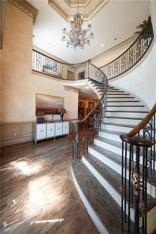 stairway featuring a towering ceiling, a wainscoted wall, ornamental molding, wood finished floors, and a notable chandelier