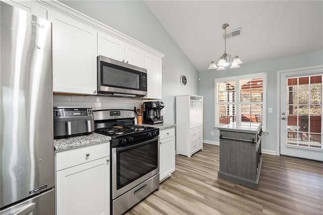 kitchen with appliances with stainless steel finishes, white cabinetry, lofted ceiling, light stone countertops, and light wood-type flooring