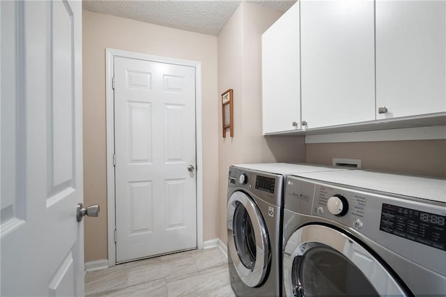 clothes washing area featuring cabinets, a textured ceiling, and washer and clothes dryer