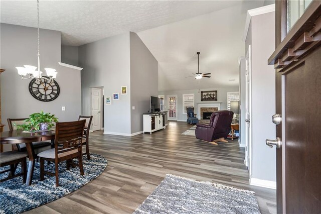 living room featuring dark wood-type flooring, a fireplace, high vaulted ceiling, and ceiling fan with notable chandelier