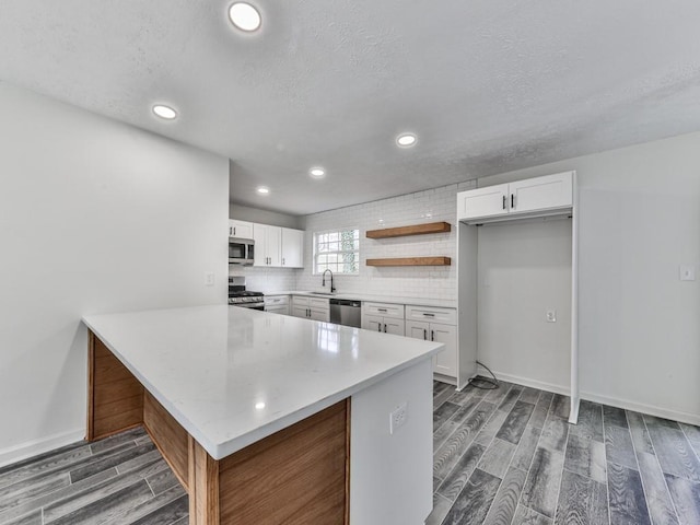 kitchen with kitchen peninsula, appliances with stainless steel finishes, white cabinetry, and sink