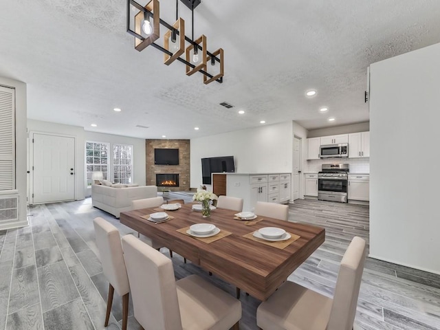 dining room featuring a fireplace, a textured ceiling, and light wood-type flooring