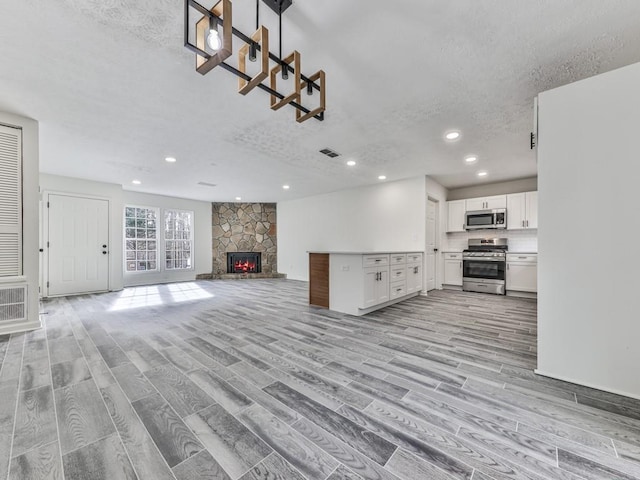 unfurnished living room featuring a textured ceiling, light hardwood / wood-style floors, and a stone fireplace