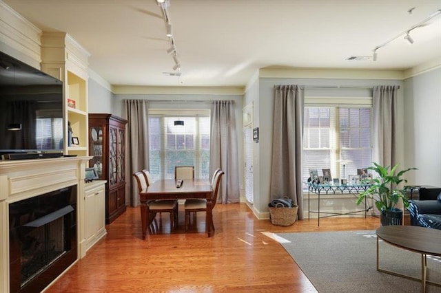 dining space with wood-type flooring, rail lighting, a wealth of natural light, and ornamental molding