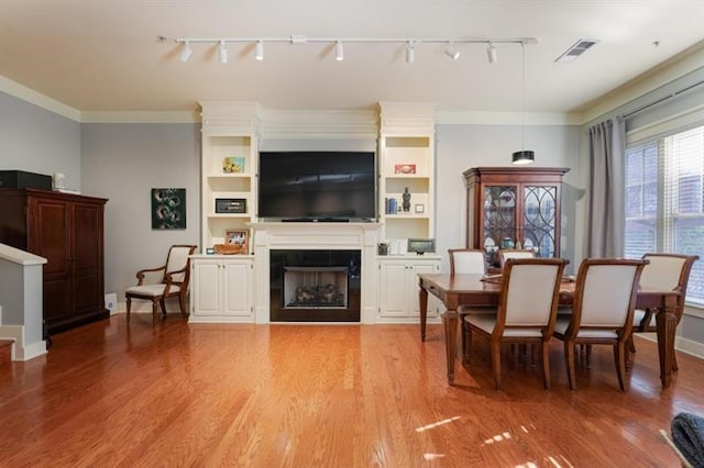 dining area with rail lighting, a tile fireplace, ornamental molding, and light wood-type flooring