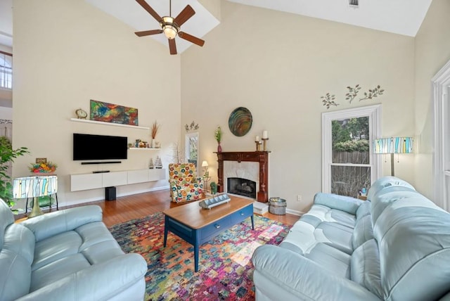 living room with baseboards, a premium fireplace, wood finished floors, high vaulted ceiling, and a ceiling fan