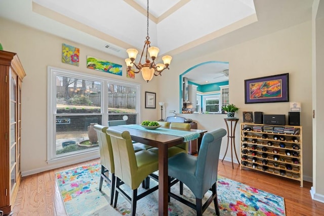 dining space with visible vents, baseboards, wood finished floors, arched walkways, and a raised ceiling