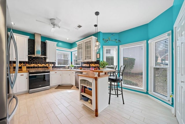 kitchen with a ceiling fan, visible vents, stainless steel appliances, decorative backsplash, and wall chimney exhaust hood