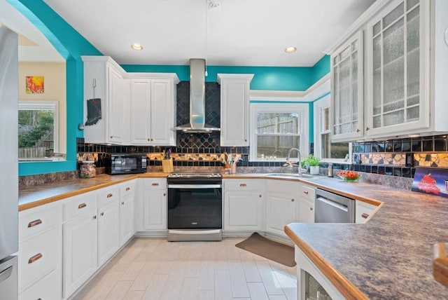 kitchen with a sink, white cabinets, appliances with stainless steel finishes, wall chimney range hood, and tasteful backsplash