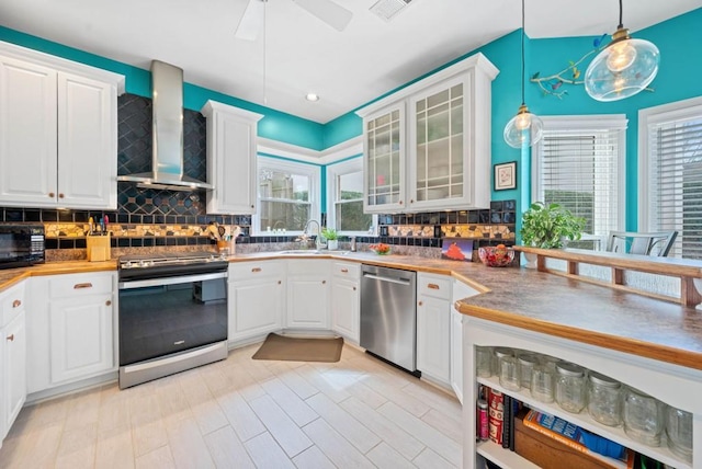 kitchen with a sink, decorative backsplash, stainless steel appliances, white cabinetry, and wall chimney exhaust hood