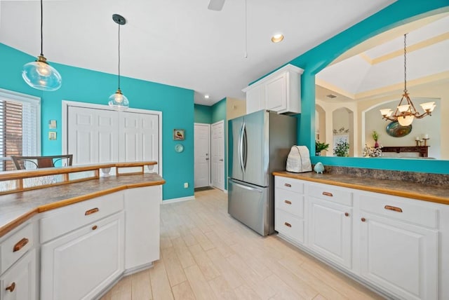 kitchen with pendant lighting, light wood-style flooring, freestanding refrigerator, a notable chandelier, and white cabinets