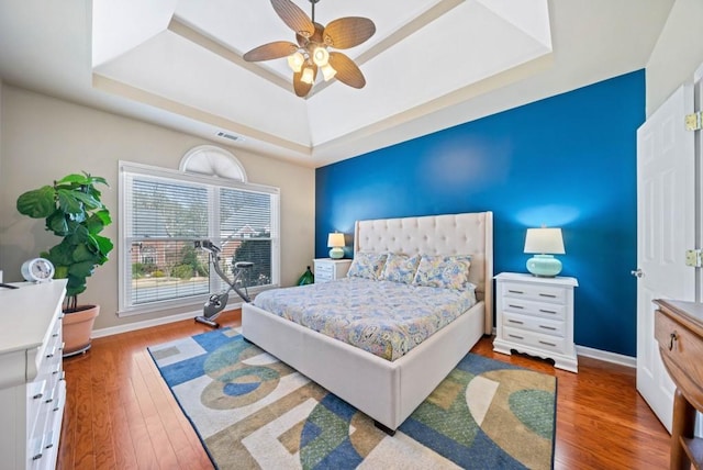 bedroom featuring a tray ceiling, hardwood / wood-style flooring, visible vents, and baseboards