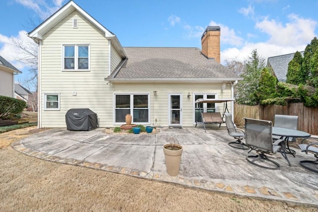 rear view of house with fence, roof with shingles, a chimney, and a patio area