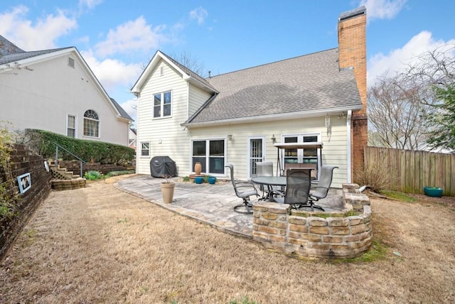 rear view of house with a patio, a shingled roof, a chimney, and fence