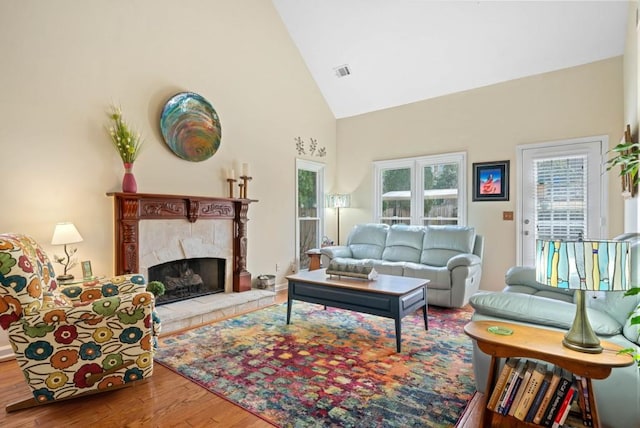 living room featuring visible vents, a fireplace, high vaulted ceiling, and wood finished floors