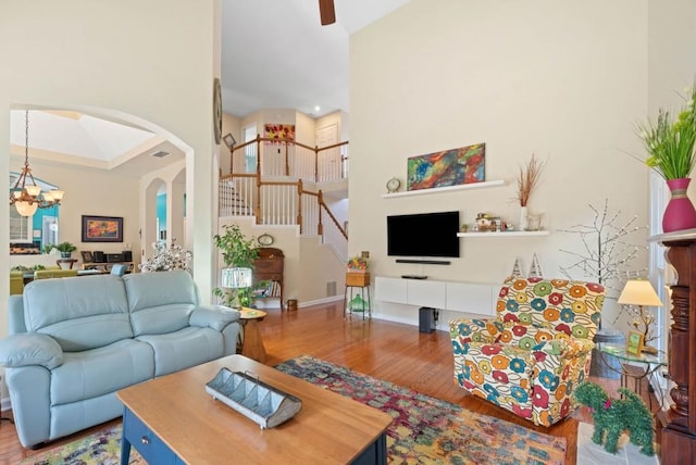 living area with stairway, wood finished floors, visible vents, a high ceiling, and arched walkways