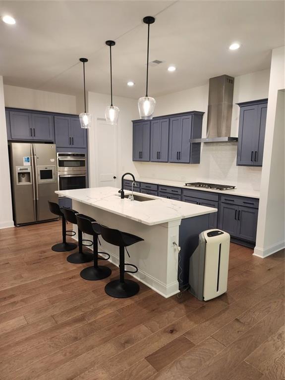 2949 Longbush, Duluth, GA 30097 - kitchen featuring appliances with stainless steel finishes, wall chimney range hood, a sink, dark wood finished floors, and a breakfast bar