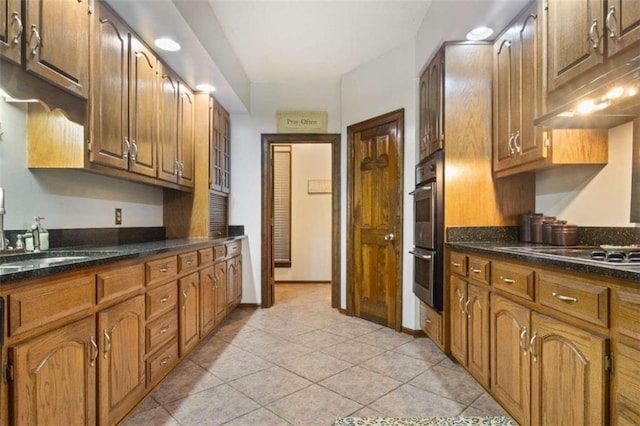 kitchen with stainless steel double oven, dark stone counters, sink, and light tile patterned floors