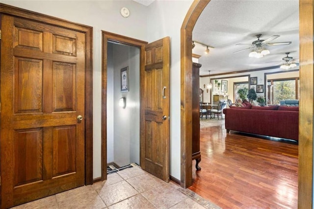 hallway with a textured ceiling, crown molding, and light hardwood / wood-style flooring