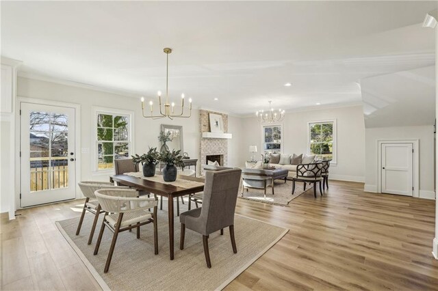 dining space featuring light wood finished floors, a fireplace, crown molding, and an inviting chandelier