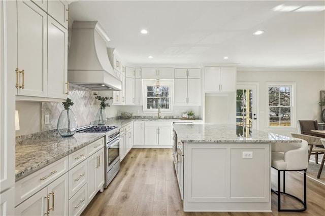 kitchen with premium range hood, light wood-style flooring, a sink, a center island, and high end range