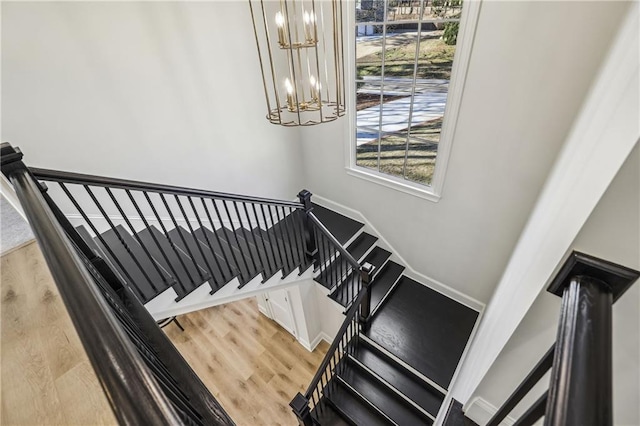 staircase featuring an inviting chandelier, baseboards, and wood finished floors