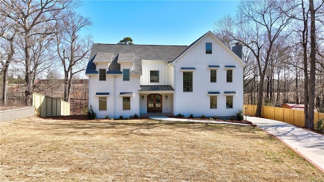 modern farmhouse featuring a standing seam roof, fence, french doors, board and batten siding, and a chimney