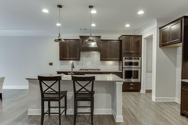 kitchen featuring light wood-style flooring, a sink, dark brown cabinetry, appliances with stainless steel finishes, and backsplash