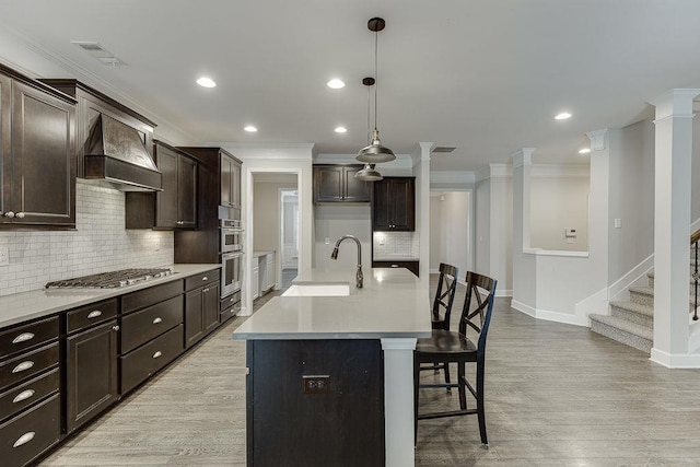 kitchen with visible vents, light wood finished floors, ornamental molding, a sink, and custom range hood