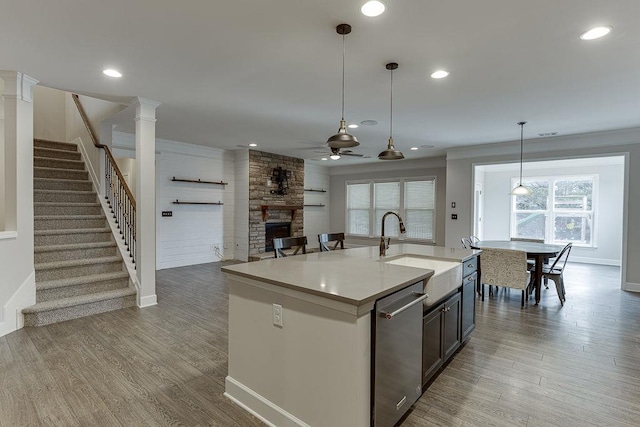 kitchen with wood finished floors, ceiling fan, a stone fireplace, a sink, and stainless steel dishwasher