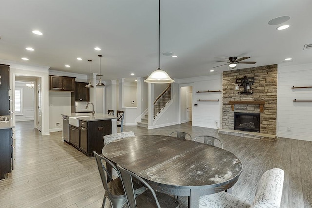 dining area with a stone fireplace, stairway, light wood-style floors, and ceiling fan