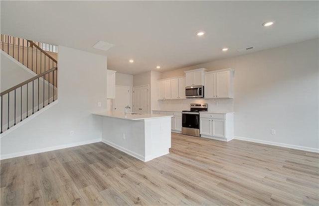 kitchen with stainless steel appliances, white cabinetry, light hardwood / wood-style flooring, and kitchen peninsula