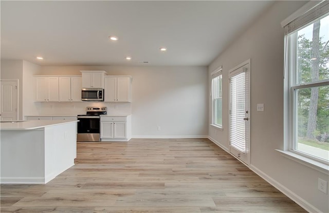 kitchen with stainless steel appliances, white cabinets, and light wood-type flooring