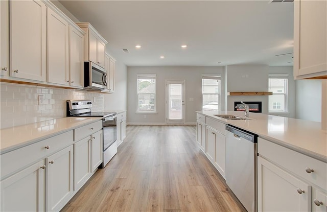 kitchen with backsplash, appliances with stainless steel finishes, sink, and light hardwood / wood-style floors