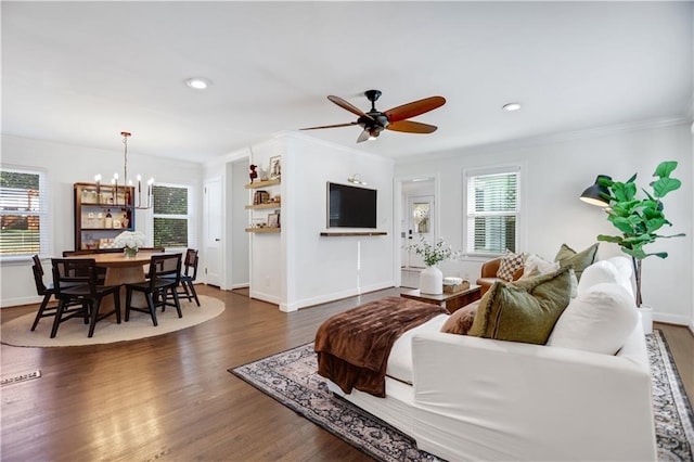 living room featuring ceiling fan with notable chandelier, dark wood-type flooring, and crown molding