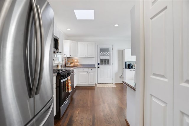 kitchen with appliances with stainless steel finishes, a skylight, dark wood-type flooring, white cabinets, and sink