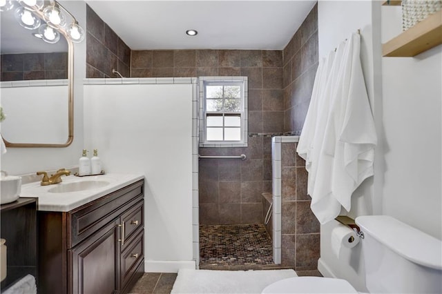 bathroom featuring vanity, toilet, tiled shower, and tile patterned flooring