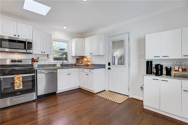 kitchen featuring stainless steel appliances, a skylight, dark wood-type flooring, sink, and white cabinetry