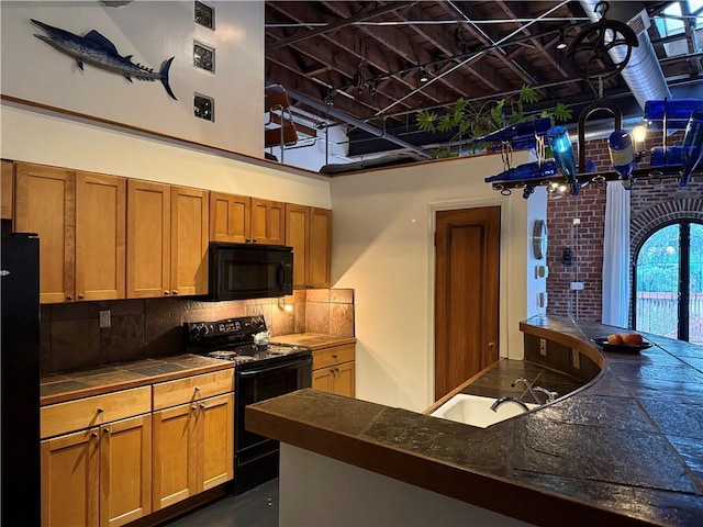 kitchen featuring brown cabinets, black appliances, a sink, backsplash, and tile counters