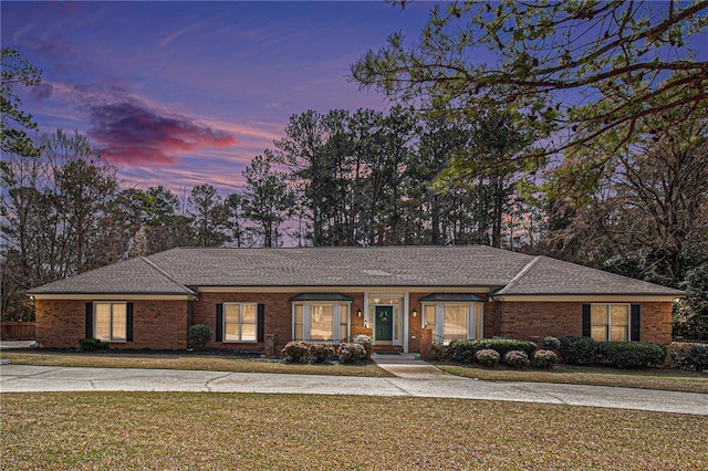 ranch-style home featuring roof with shingles, a front lawn, and brick siding