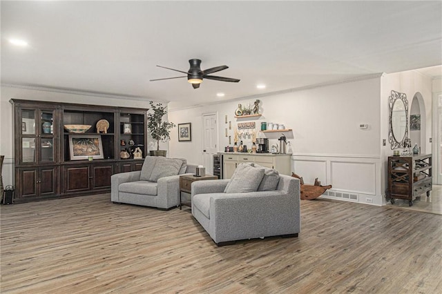 living room featuring visible vents, a decorative wall, ornamental molding, a bar, and light wood-type flooring