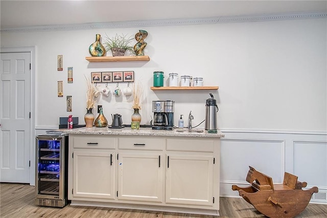 bar featuring wine cooler, a dry bar, light wood-style floors, wainscoting, and a sink