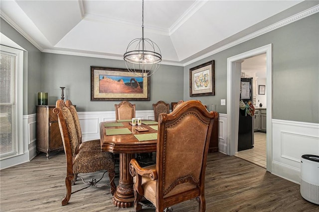 dining room with a notable chandelier, a wainscoted wall, wood finished floors, a raised ceiling, and crown molding