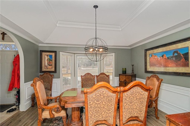 dining space featuring an inviting chandelier, a raised ceiling, wood finished floors, and wainscoting